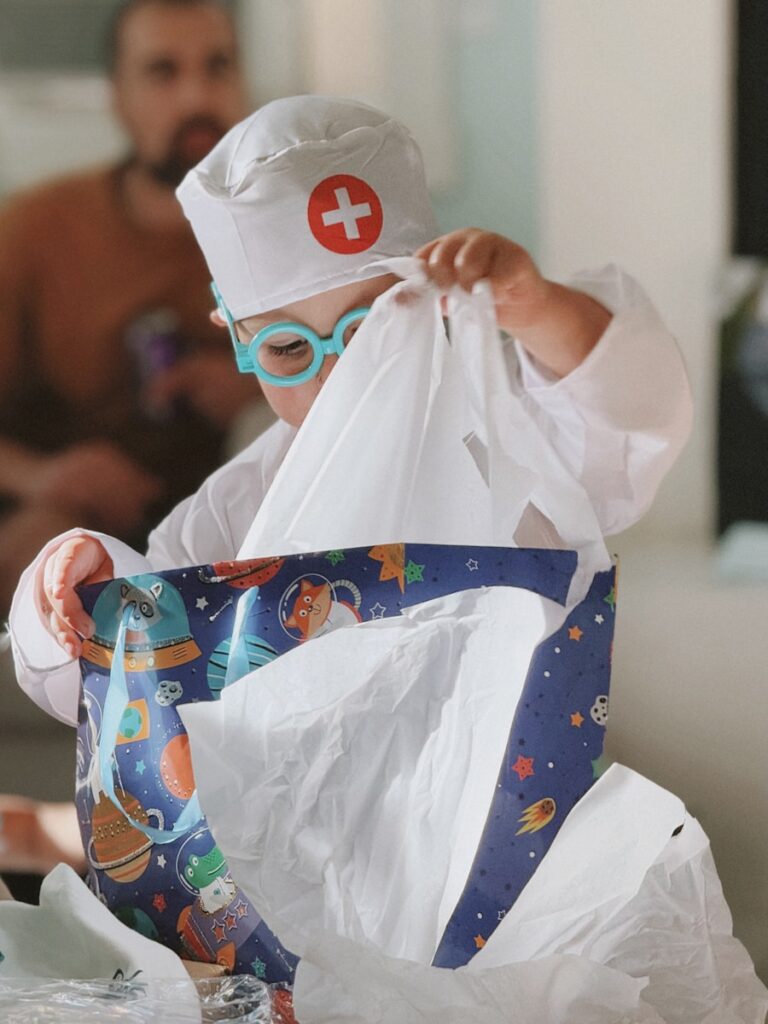 Child in doctor costume opening a gift bag.